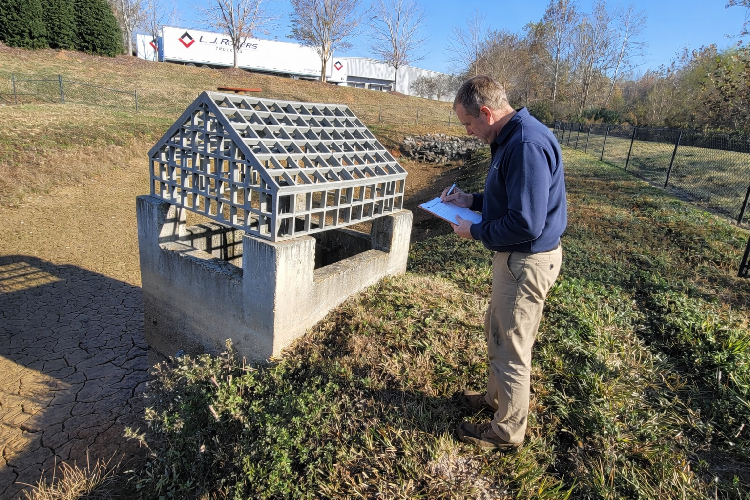 Certified inspector conducting stormwater compliance inspection at detention pond and outlet control structure